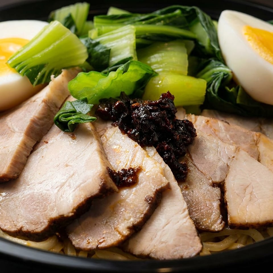 Black bowl of sliced pork over noodles, topped with leafy greens, halved soft-boiled eggs, and dark sauce.