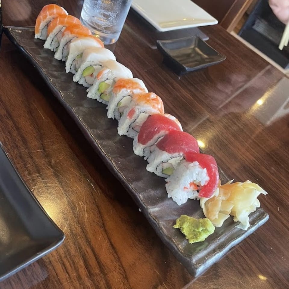 Assorted sushi rolls arranged on a long black platter with wasabi, pickled ginger, dipping sauce, and water.