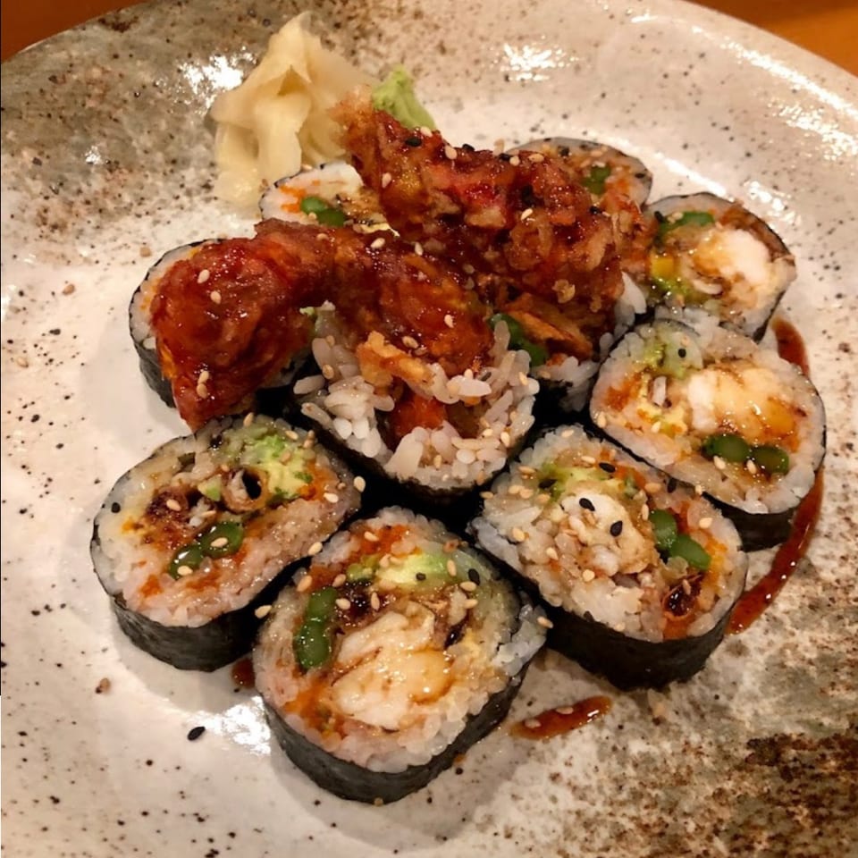 Sushi rolls filled with shrimp, avocado, and vegetables, topped with crispy glazed shrimp and sesame seeds on a ceramic plate.