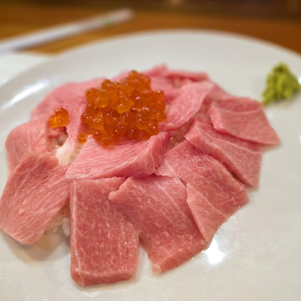 Marbled pink tuna slices arranged over rice, topped with orange fish roe and served with wasabi on a white plate.