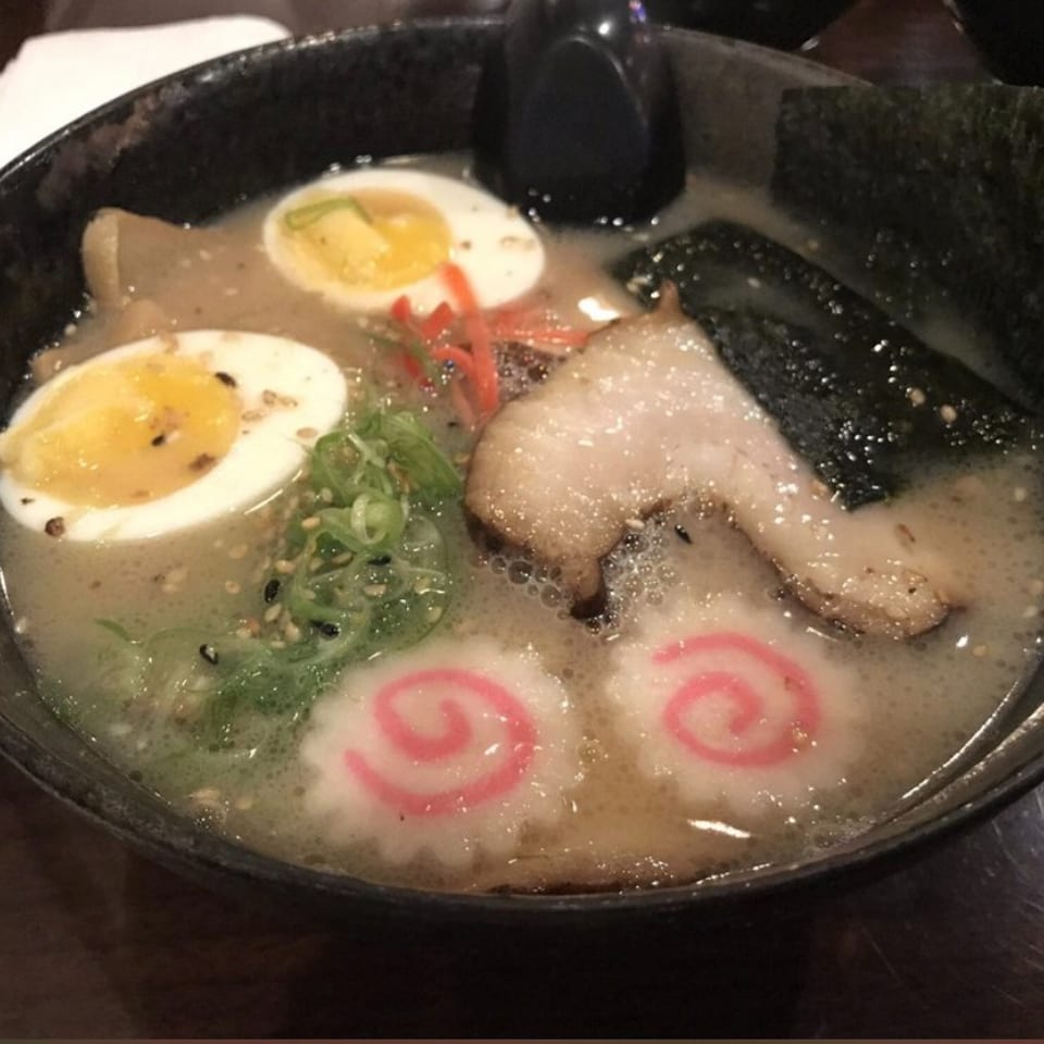 Bowl of creamy ramen topped with sliced pork, soft-boiled eggs, seaweed, scallions, and pink fish cakes.