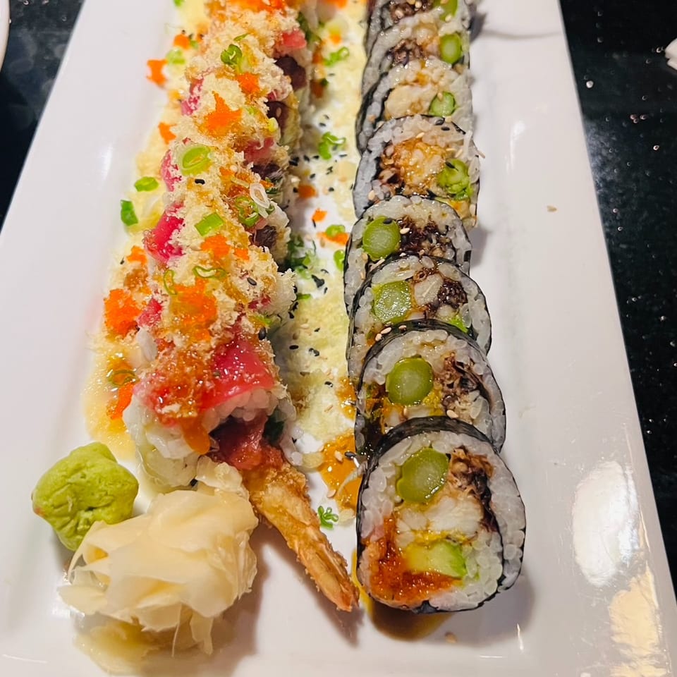 Assorted sushi rolls topped with orange roe and scallions, served with fried squid, wasabi, and pickled ginger on a white plate.