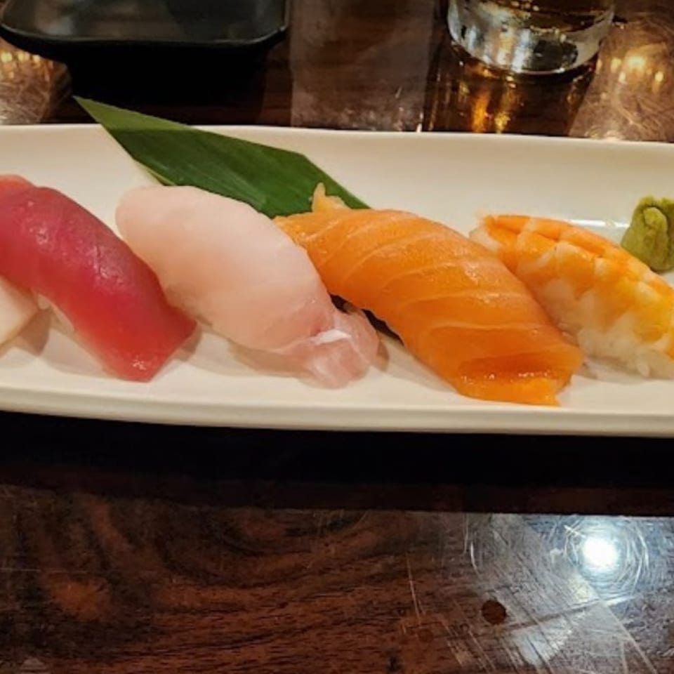 Plate of assorted sushi nigiri, including white fish, tuna, salmon, and shrimp, with wasabi and pickled ginger.