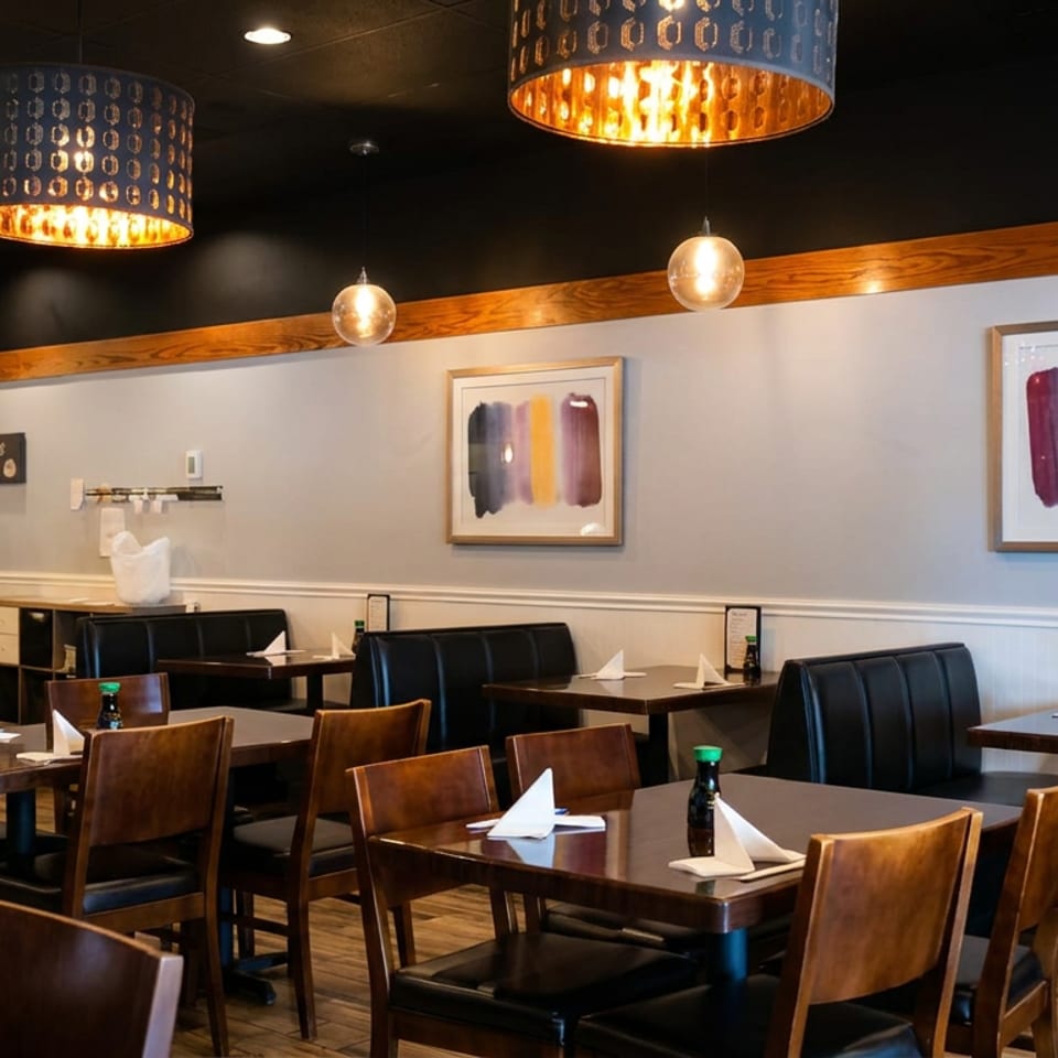 Warmly lit restaurant dining room with neatly set tables, leather booths, pendant lights, and abstract wall art.