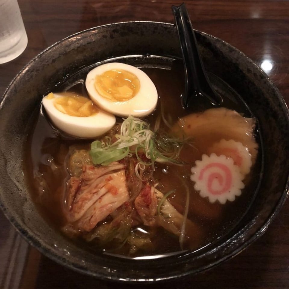 Japanese ramen bowl with dark broth, sliced soft-boiled egg, shrimp, pork, scallions, and narutomaki fish cake.