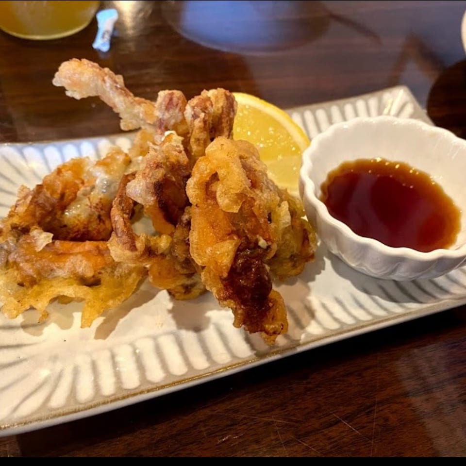 Crispy fried seafood and vegetables served on a rectangular plate with lemon wedge and dipping sauce.